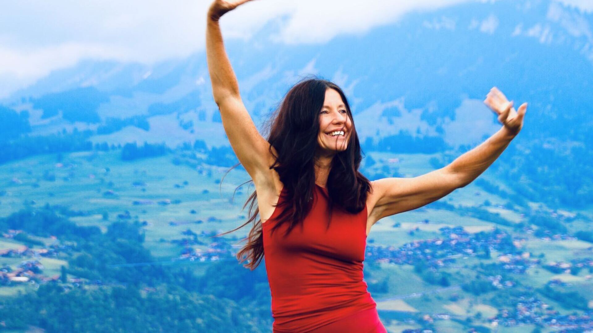 Yogalehrerin Claudia Eva Reinig in roter Yogakleidung mit wehenden Haaren und freudiger Position 