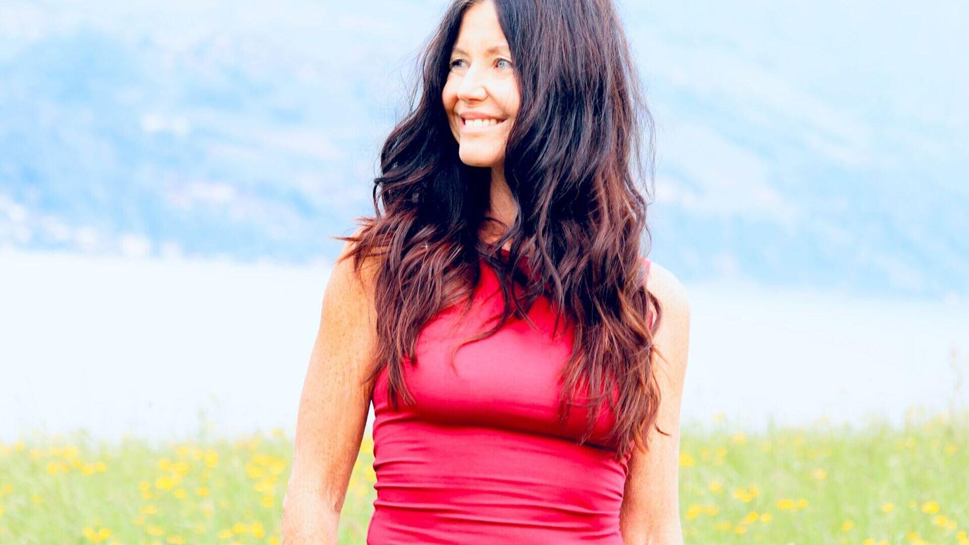Yogalehrerin Claudia Eva Reinig in roter Yogakleidung mit wehenden Haaren und freudiger Position 