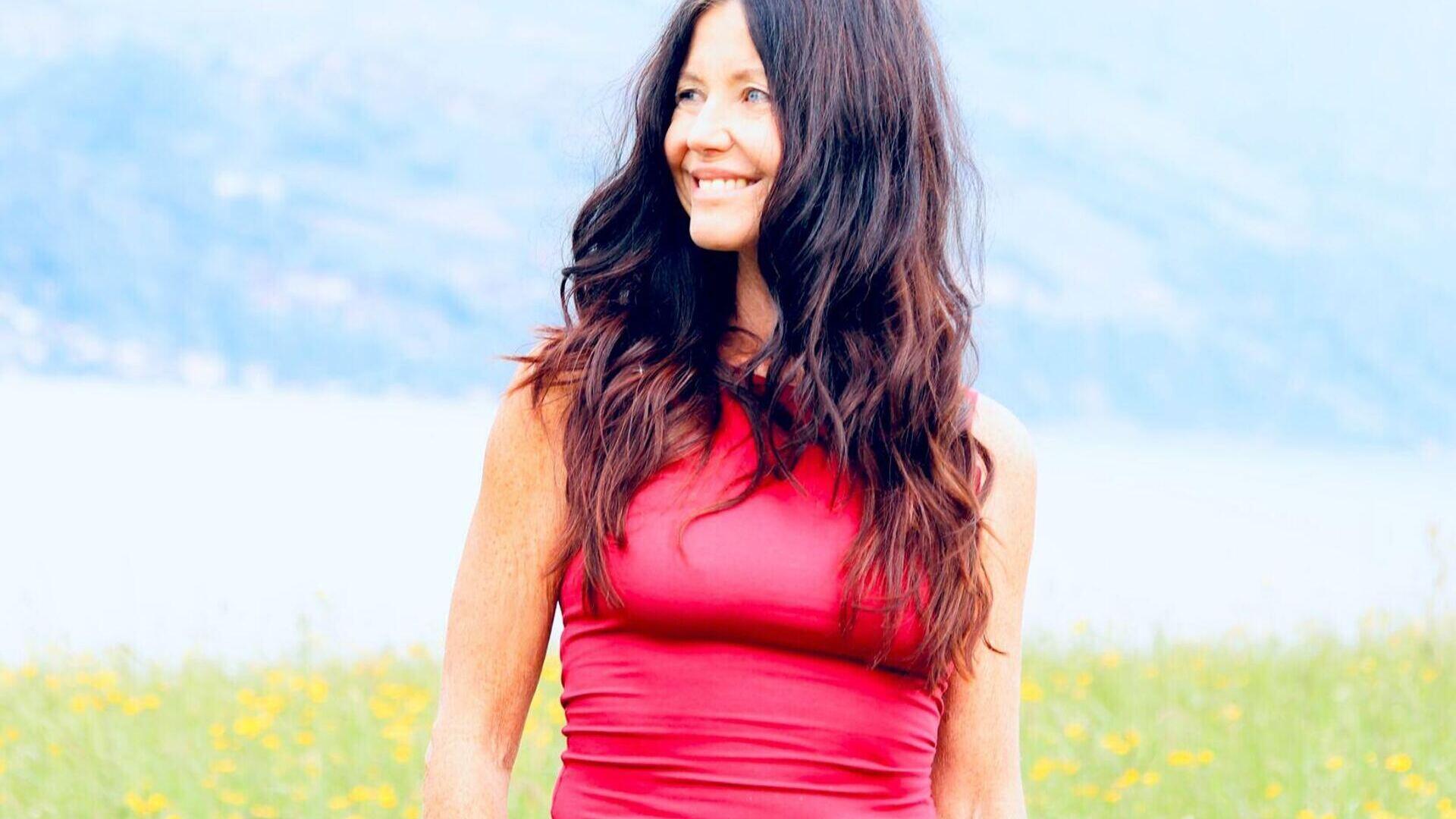 Yogalehrerin Claudia Eva Reinig in roter Yogakleidung vor Wiese und See