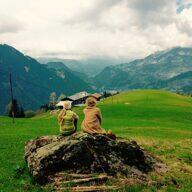 Zwei Frauen sitzen auf einem Stein vor den Bergen