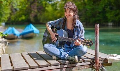 Yogalehrerin Sarah Zaugg mit Gitarre auf einem Seesteg, im Hintergrund der Thunersee und Boote