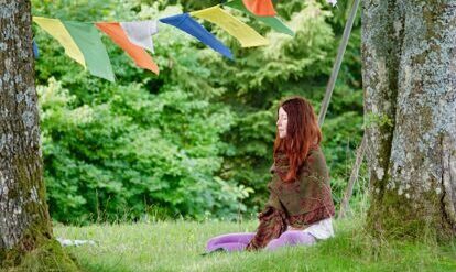 Claudia Eva Reinig meditierend unter Baum, mit tibetischen Gebetsfahnen
