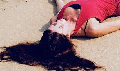 Claudia Eva Reinig liegt am Strand in roter Yogakleidung und praktiziert Yoga Nidra Entspannung