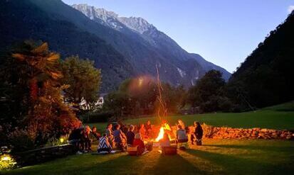Tessin: Yoga, Meditation und Mantra am Lagerfeuer, im Hintergrund der Lichtschein der untergehende Sonne und Berge