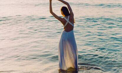 Frau im langem Kleid in Yogaposition am Mehr