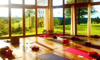 Yogaraum mit Yogamatten mit grosser Glasfront, Sicht in die Natur, Sonne scheint