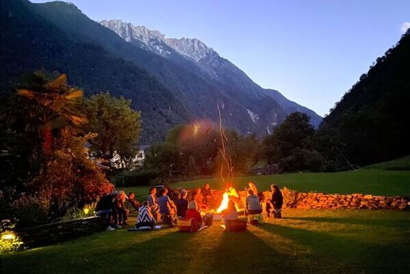Yoga, Meditation und Mantra am Lagerfeuer, im Hintergrund der Lichtschein der untergehende Sonne und Berge