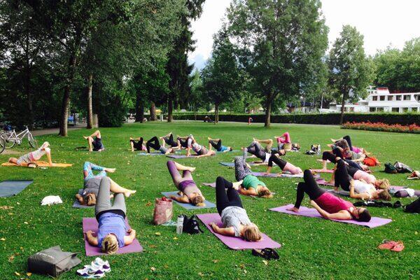 Yogaübende im Park in Thun, in der Yogastellung Schulterbrücke, im Hintergrund Bäume