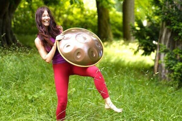 Claudia Eva Reinig in roter Yogakleidung und mit Handpan auf einer Wiese im Schadaupark in Thun, Schweiz