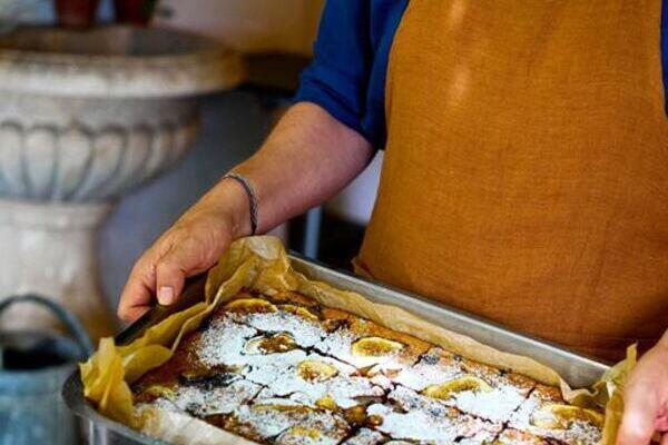 Koch mit rostfarbener Schürze bringt selbst gebackenen Kuchen auf dem Blech