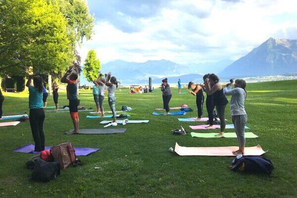 Yogapraktizierende im Park, links Bäume, im Hintergrund der Thunersee und Berg Niesen