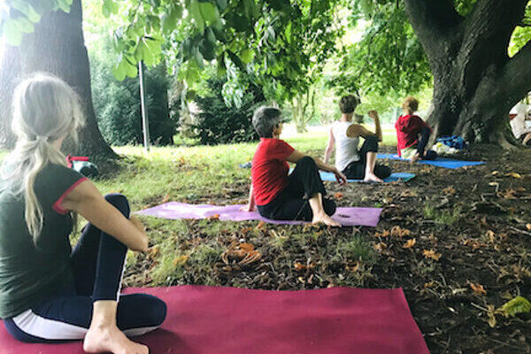 Yogaübende im Freien in der Yogaposition Drehsitz, im Sommer in Thun unter Bäumen