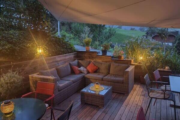Sitzplatz im Freien mit Korbmöbel, Kissen und Lampen am Abend