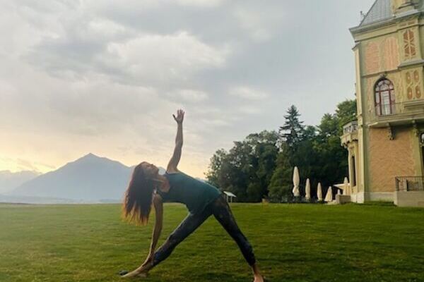 Yogalehrerin Claudia Reinig in der Dreiecksstellung im Freien im Sommer in Thun im Schadaupark, im Hintergrund der Berg Niesen und das Schloss Schadau
