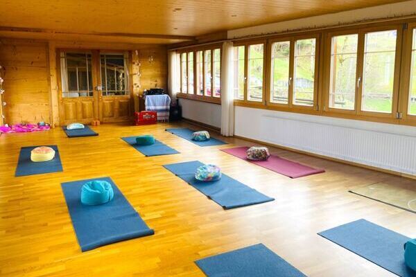 Yogasaal mit blauen und roten Yogamatten und Sitzkissen, Fensterfront Blick in die Berge