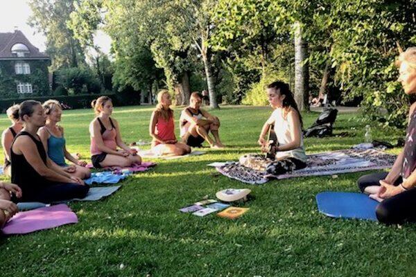 Yogaübende im Freien im Yogasitz, Sarah Zaugg spielt Gitarre