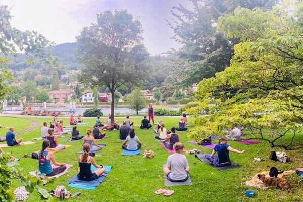 Yogaübende im Freien, sitzend auf der Wiese, im Hintergrund Bäume