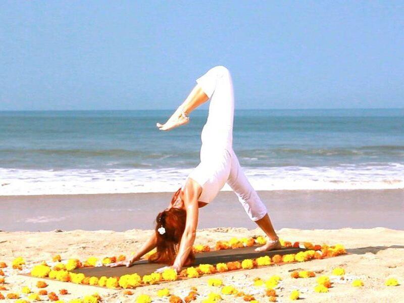 Claudia Eva Reinig zeigt Yogaposition Hund abschauend mit gehobenem Bein, im Hintergrund das Meer