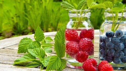Gläser mit Wasser und Himbeeren und Heidelbeeren zum Trinken auf einem Holztisch