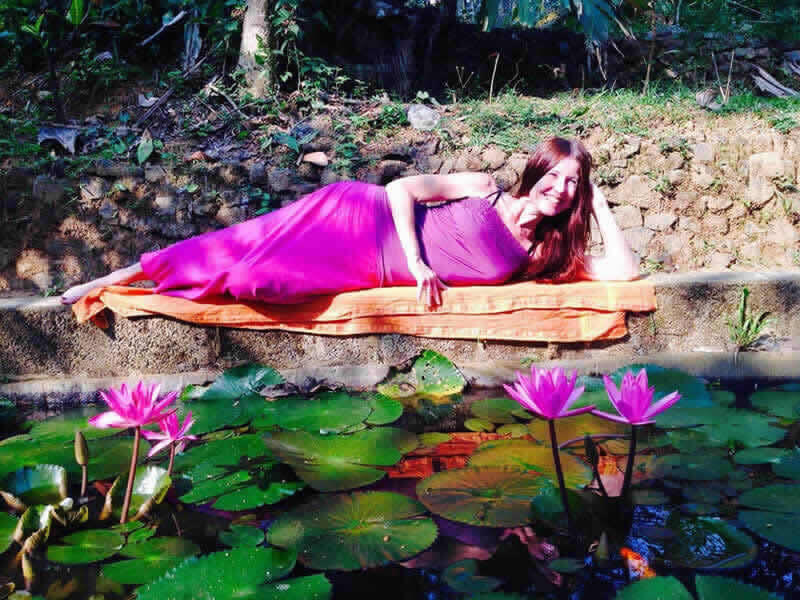 Claudia Eva Reinig praktiziert Yoga Nidra in einem pinkfarbenen Kleid an einem Lotusteich
